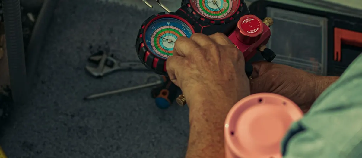 Technician adjusting refrigerant manifold gauges during a maintenance tune-up