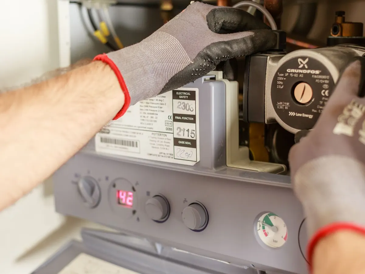 Gloved hands adjusting a boiler pump and gauges during heating service