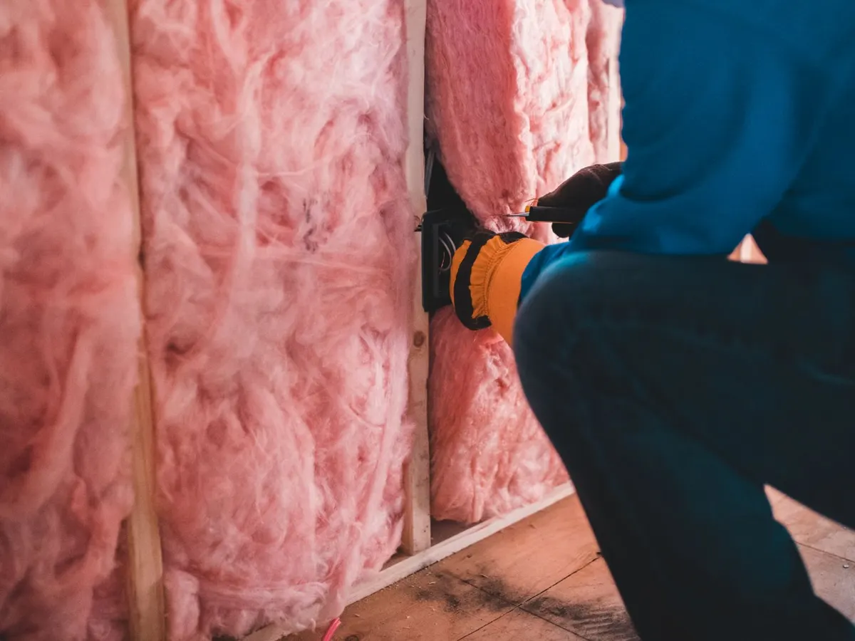 Worker installing insulation batts between wall studs